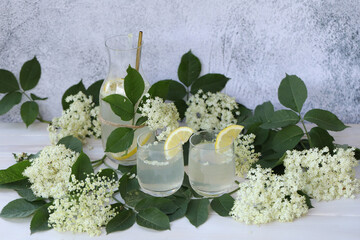 Glass and bottle of lemonade with elder flowers. On light grey background with copy space