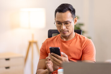 Picture of young asian man using a smartphone and smiling. working at home.accountant Documents data contract report for analysis TAX.