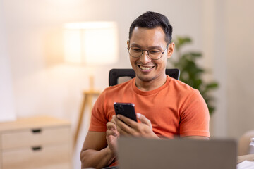 Picture of young asian man using a smartphone and smiling. working at home.accountant Documents data contract report for analysis TAX.