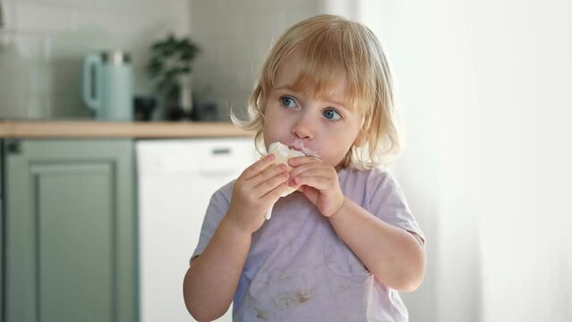 Baby girl enjoying ice cream. Pretty little toddler eating an ice-cream indoors, at home. Dining room background. Small child eats plombir and cream messy on her mouth. Cute kid with tasty sweet food.
