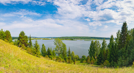 Panoramic view of the river from the hill on a sunny day, islands in the distance, clouds in the blue sky.