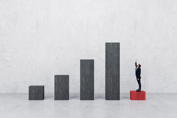 Businessman pointing up on low chart bar looking at top. Success and career growth concept. Concrete wall background.