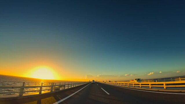 夕暮れの海の上の高速道路を走る自動車