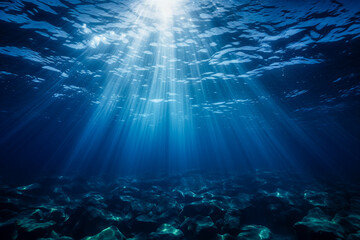Fototapeta premium Underwater ocean scene with rays of light, sun beams. Clear blue water, sea background. Seabed without life, only rocks. World water day, raise awareness for worldwide problems concerning water.