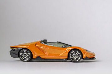 Sideview of orange toy model convertible supercar on a white background