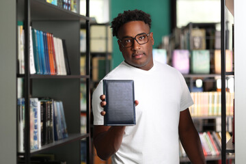 Focused Dark-skinned smart student in white t-shirt showing book in college library. Stylish...
