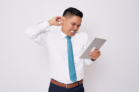 Confused young Asian man in formal wear holding a digital tablet and scratching his head isolated on white background - Powered by Adobe