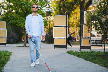 Young handsome blinded man walking with stick in town