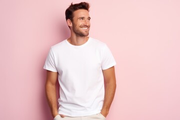 Portrait of a happy 30 - year - old man wearing a white t shirts with hands in pocket next to a light pink pastel background. Mock up t shirt concept.