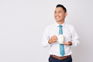 Happy smiling young Asian man in formal wear standing holding a cup of coffee, enjoying rest and looking aside, isolated on white background