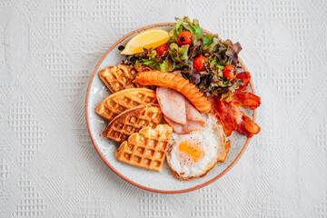 Breakfast waffles, fried eggs, bacon, ham, sausage and salad.