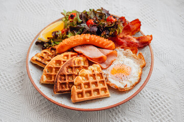 Breakfast waffles, fried eggs, bacon, ham, sausage and salad.