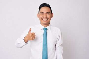 Portrait of a smiling happy successful young Asian man in formal wear standing confident while showing a thumbs up and looking at camera isolated on white background