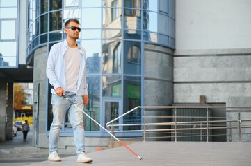 Young handsome blinded man walking with stick in town