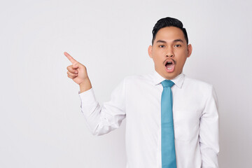 Portrait of surprised young Asian man in formal wear standing pointing fingers aside at copy space for advertisement and open mouth isolated on white background