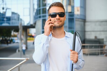 Young blind man with smartphone in city, calling