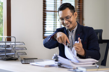 Happy Excited Young business Asian man working at workplace with laptop and papers on desk