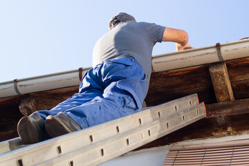 bricklayer construction worker on metalic staircase to repair old tile roof - obrazy, fototapety, plakaty