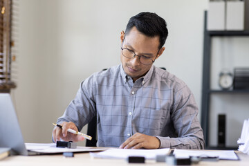 Obraz premium Serious and focused financier accountant on paper work inside office, mature business asian man using calculator and laptop for calculating reports and summarizing accounts, 