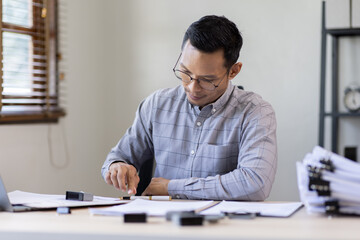 Serious and focused financier accountant on paper work inside office, mature business asian man using calculator and laptop for calculating reports and summarizing accounts, 