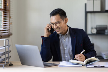 Obraz premium Inspiring productivity with a wealth of technology. Shot of a young business asian man talking on his phone and using a laptop during a late night at work.