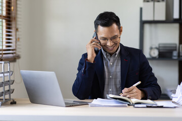 Obraz premium Inspiring productivity with a wealth of technology. Shot of a young business asian man talking on his phone and using a laptop during a late night at work.