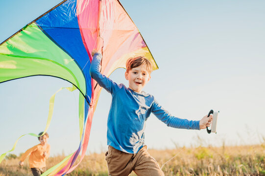 Smiling boy holding kite with brother running in field under sky