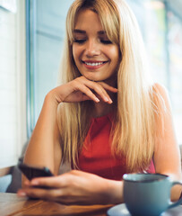 Young smiling woman browsing smartphone in cafe