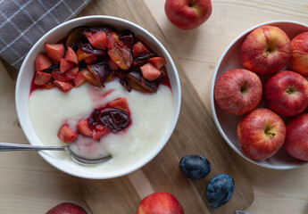 Winter breakfast with a warm semolina porridge and cooked apples and plums with honey on a plate.