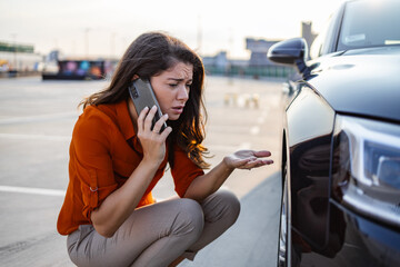 Naklejka premium Woman calling for assistance with flat tire on car in the city. Young woman with high heels in the city with flat tire, frustrated near broken car