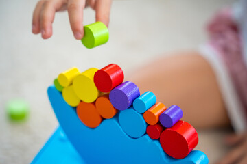 Little girl playing with wooden balancing toy on the floor in home living room. Focus on balancer