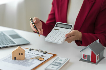 A young Asian real estate agent is reviewing documents and calculating interest rates to inform tenants of monthly installments before entering into contracts to buy or sell real estate. - obrazy, fototapety, plakaty