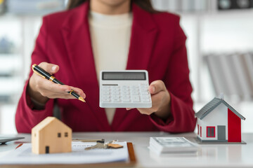 A young Asian real estate agent is reviewing documents and calculating interest rates to inform...