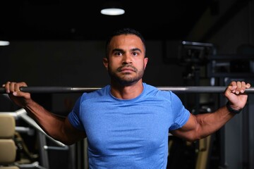 Fototapeta premium Portrait of a strong Hispanic man weightlifting at a gym.