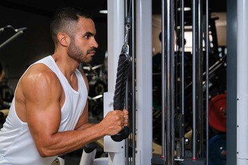 Strong Hispanic man doing cable rope pullovers at a gym.