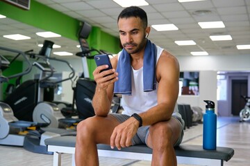 Fototapeta na wymiar Strong Hispanic man listening music on his smartphone at a gym.