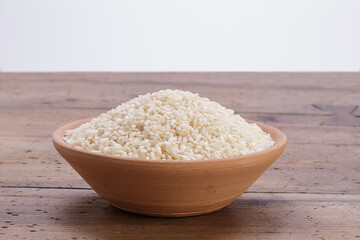 white rice inside a terracotta bowl on rustic wooden table with white background