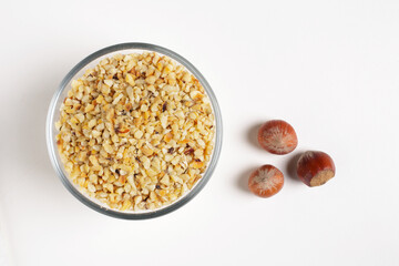 chopped hazelnuts in a glass bowl with hazelnuts in shell on a white background shot from above