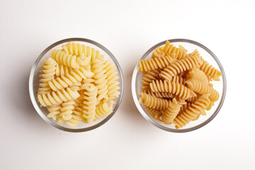 composition of durum wheat and wholemeal pasta in glass bowl on white background top view