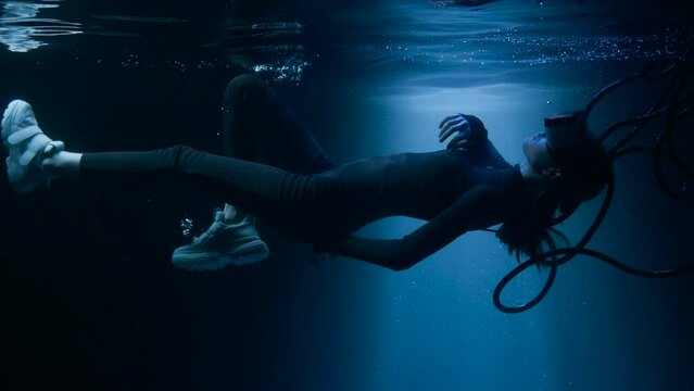 Beautiful woman with flowing hair in futuristic dress under the water. Girl in glasses of virtual reality. Augmented reality, game, future technology concept. VR.
