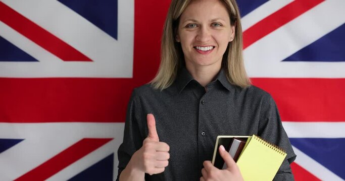 Woman holding english textbooks and showing thumb up against background of UK flag 4k movie slow motion. Foreign language school concept 
