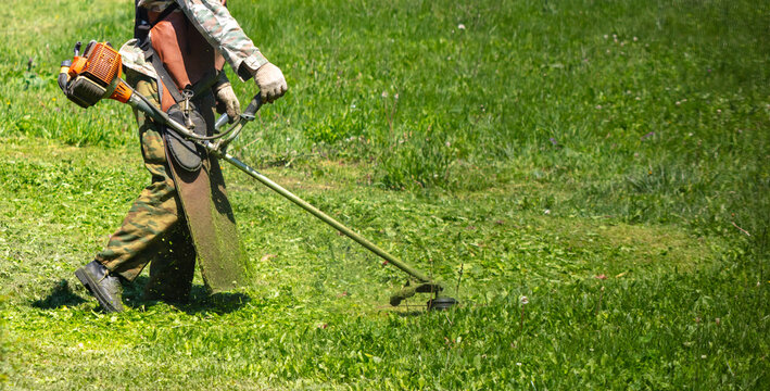 A man mows green grass with a petrol trimmer