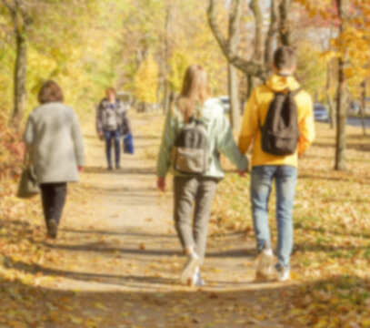 Defocused image of an autumn park with trees, foliage and paths with fallen leaves and people.