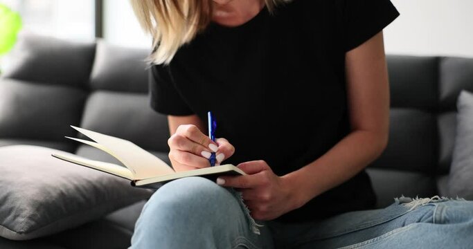 Woman writing notes with ballpoint pen in notepad on sofa at home closeup 4k movie. Planning and organizing cases and keeping diary concept