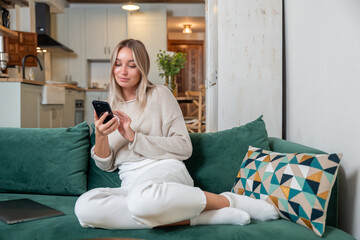 Caucasian woman with blonde hair using her phone while sitting on sofa at home