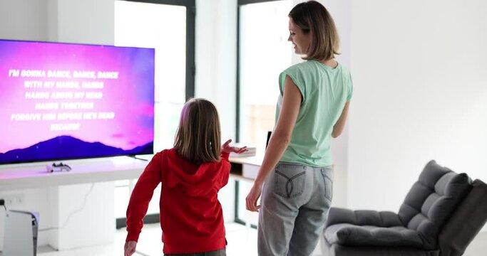 Mom and daughter dancing near tv at home back view 4k movie slow motion. Entertainment with children concept