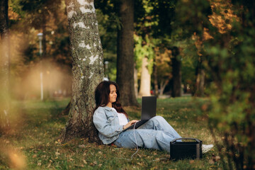 Fototapeta premium A woman in nature works on a laptop charging from a portable charging station