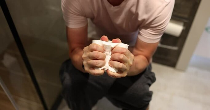 Man with hemorrhoids and painful bowel movements squeezing roll of toilet paper 4k movie. Prevention and treatment of constipation concept