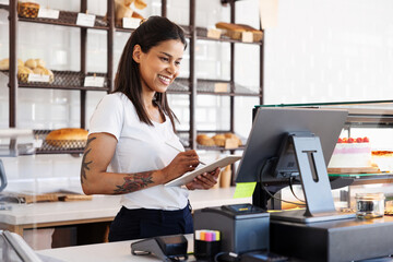 Smiling woman working in cafe bakery, using digital tablet and cash computer