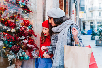 Women looking at a store window at Christmas with shopping bags on the street in winter sales.